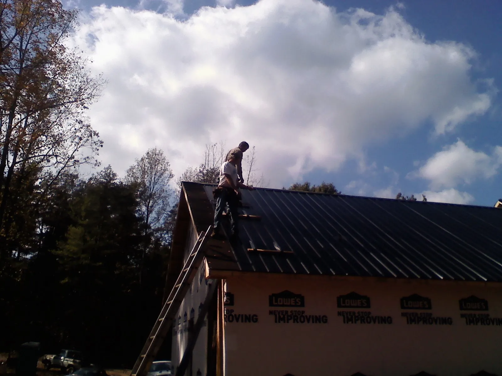 Roofer fastening dark metal panels high against a cloudy sky, from a Roof Inspection job in Moclips